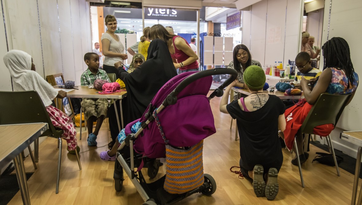 Children (some in buggies) and adults clustered around tables working on small manual tasks.