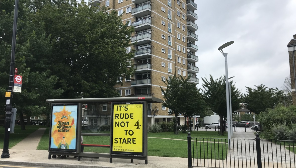 A bus shelter in front of a high-rise block of flats, with an advert for Channel 4's Paralympic coverage. In bold black type on a yellow background it reds 'It's Rude Not to Stare', along with the Channel 4 logo. The bus stop sign contains the traditional