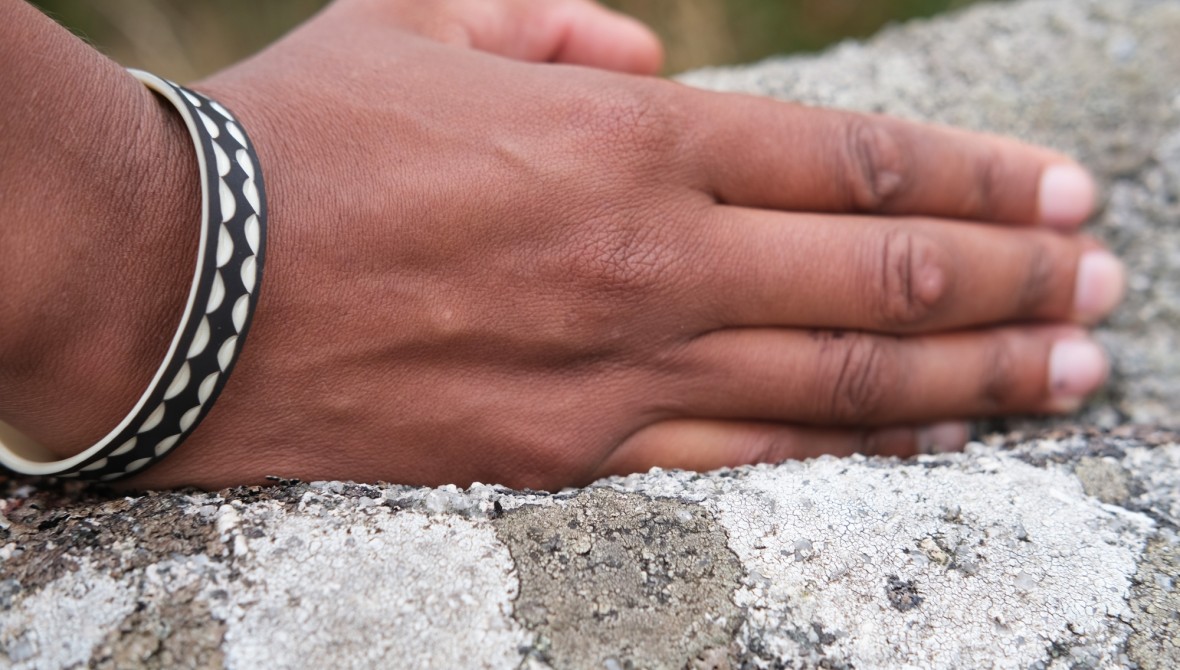 A hand with a black and white bracelet around the wrist, facing downwards on top of a rock